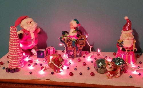 Christmas display with pink string lights, Santa figures, and festive ornaments on a white surface.