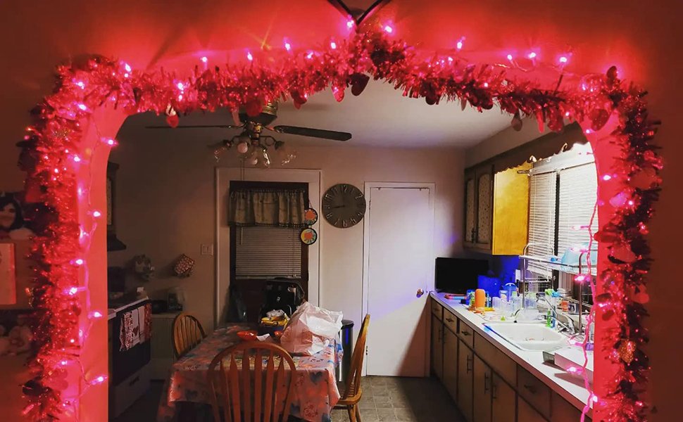 Pink string lights and tinsel draped over a doorway in a kitchen setting, with a table and chairs visible.