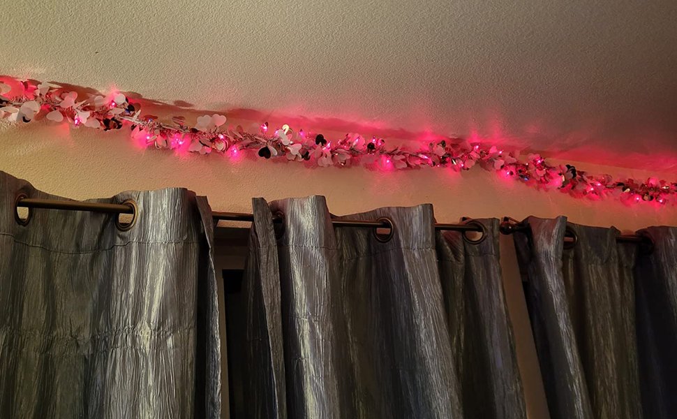 Pink string lights with heart-shaped decorations draped along a ceiling above grey curtains.