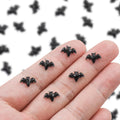 Hand holding several miniature black resin bats against a blurred background of more bats.