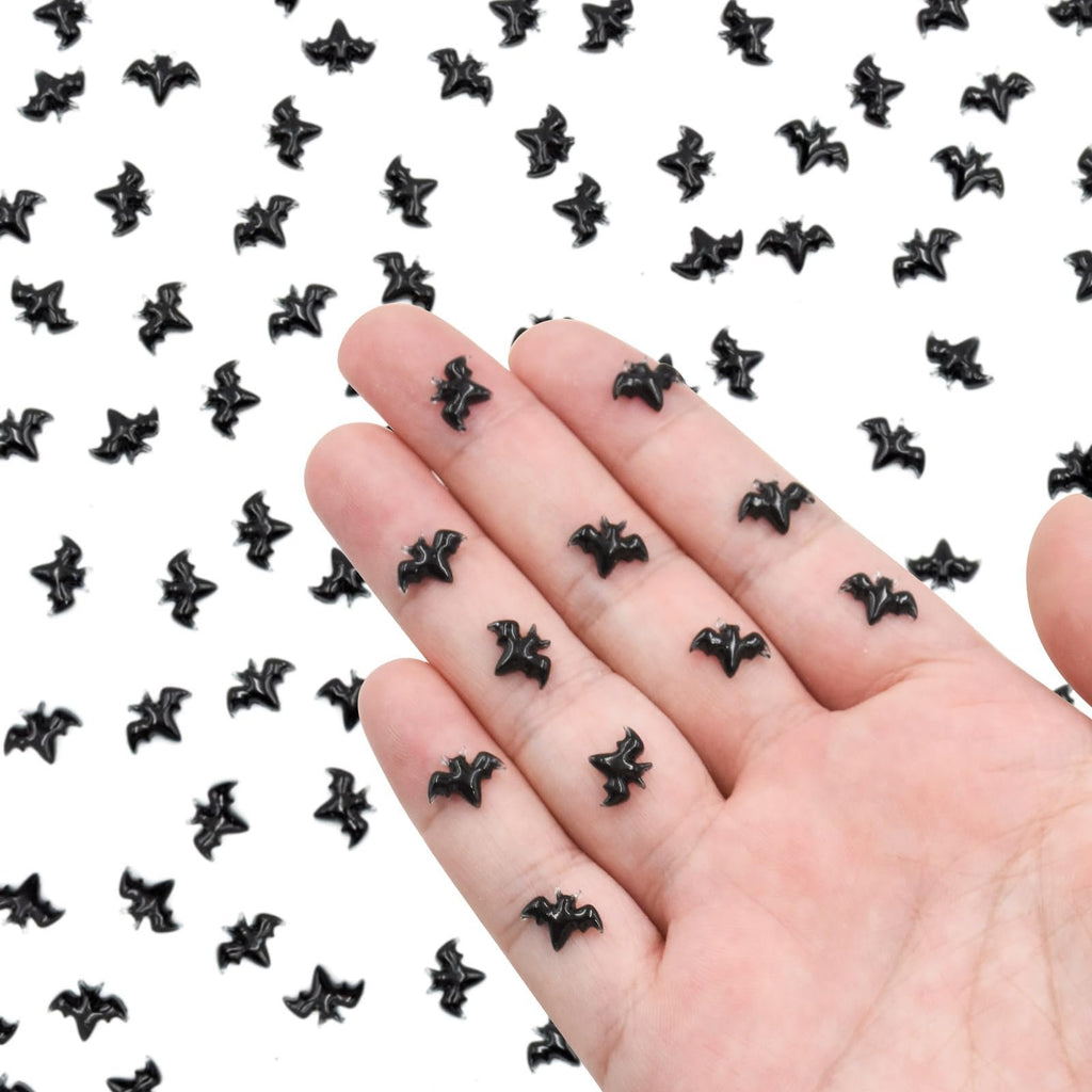 Hand holding miniature black resin bats, scattered on a white background