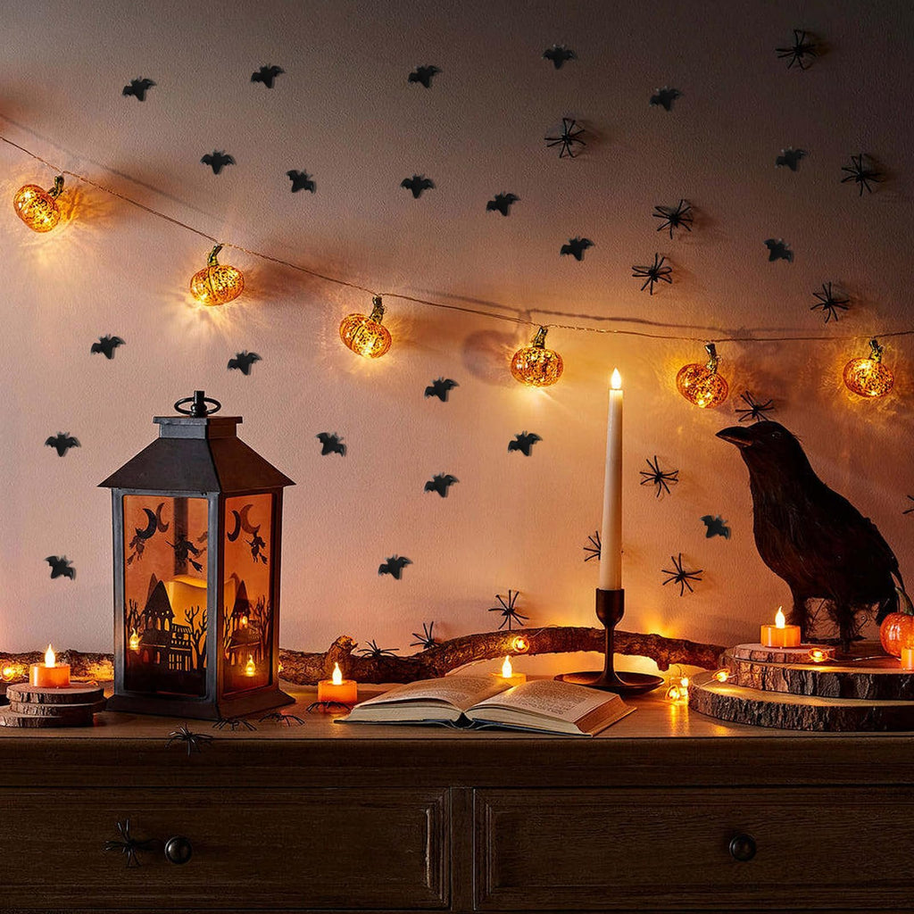 Halloween scene with miniature bats and spiders on wall, pumpkin string lights, a lantern, a crow, and candles.