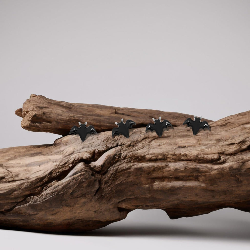 Four black miniature bats perched on a piece of weathered driftwood against a light gray background.