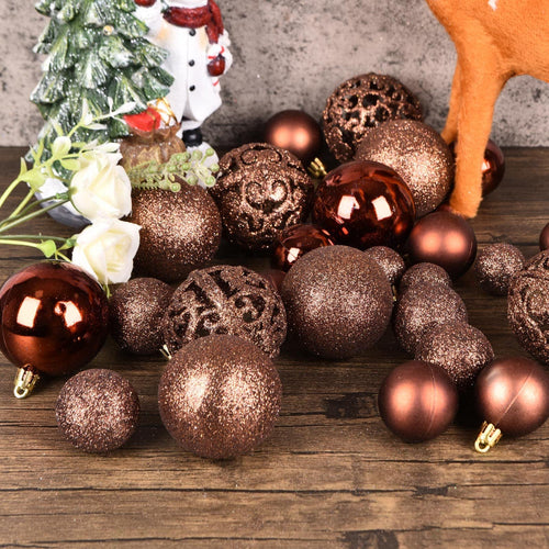 Assortment of brown shatterproof Christmas ball ornaments scattered on a wooden surface with a snowman figurine and white flowers in the background.