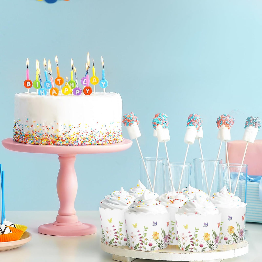 Birthday cake with colorful candles and frosted cupcakes with floral wrappers