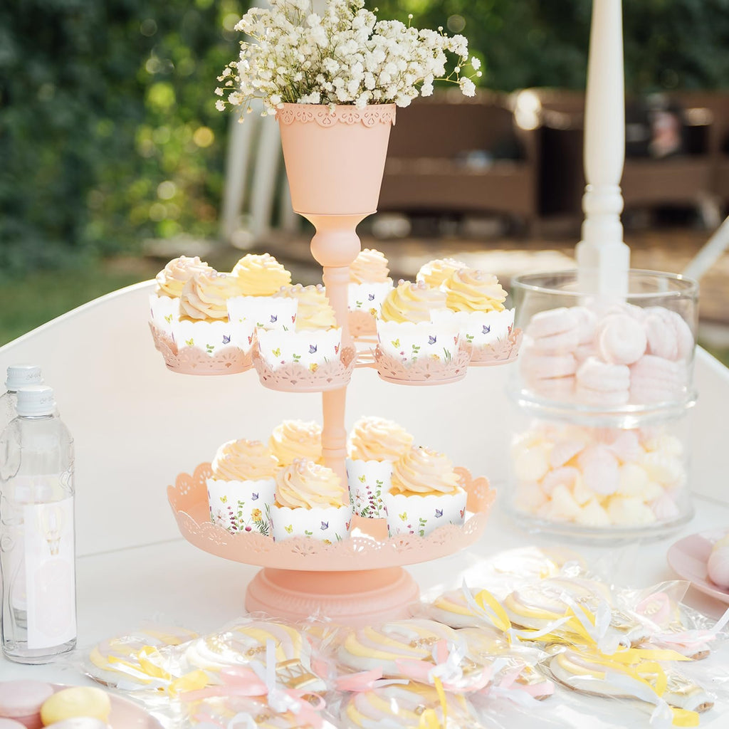 Cupcakes with floral and butterfly wrappers on a pink tiered stand, with cookies and marshmallows nearby.
