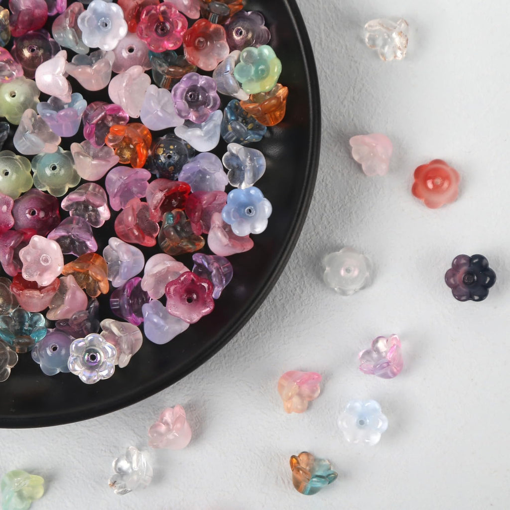 Assortment of colorful glass flower beads scattered on a white surface and a black plate.