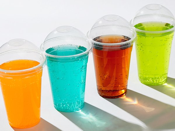 Four clear plastic cups with dome lids filled with colorful beverages on a white background.