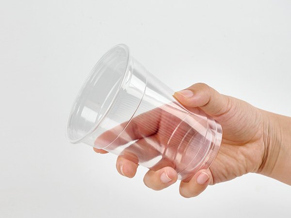 Hand holding a clear disposable plastic cup against a white background