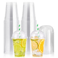 Two clear plastic cups with dome lids and striped straws filled with ice and citrus slices, next to stacks of empty cups and lids.
