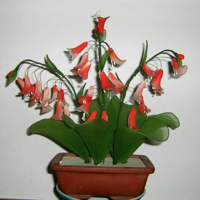 Artificial red and pink bell flowers in a terracotta pot against a white background