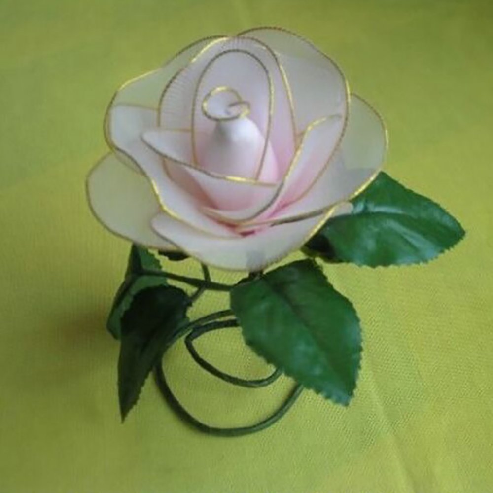Close-up of a delicate pink and white fabric rose with gold trim, on a green wire stem with leaves, against a yellow background.
