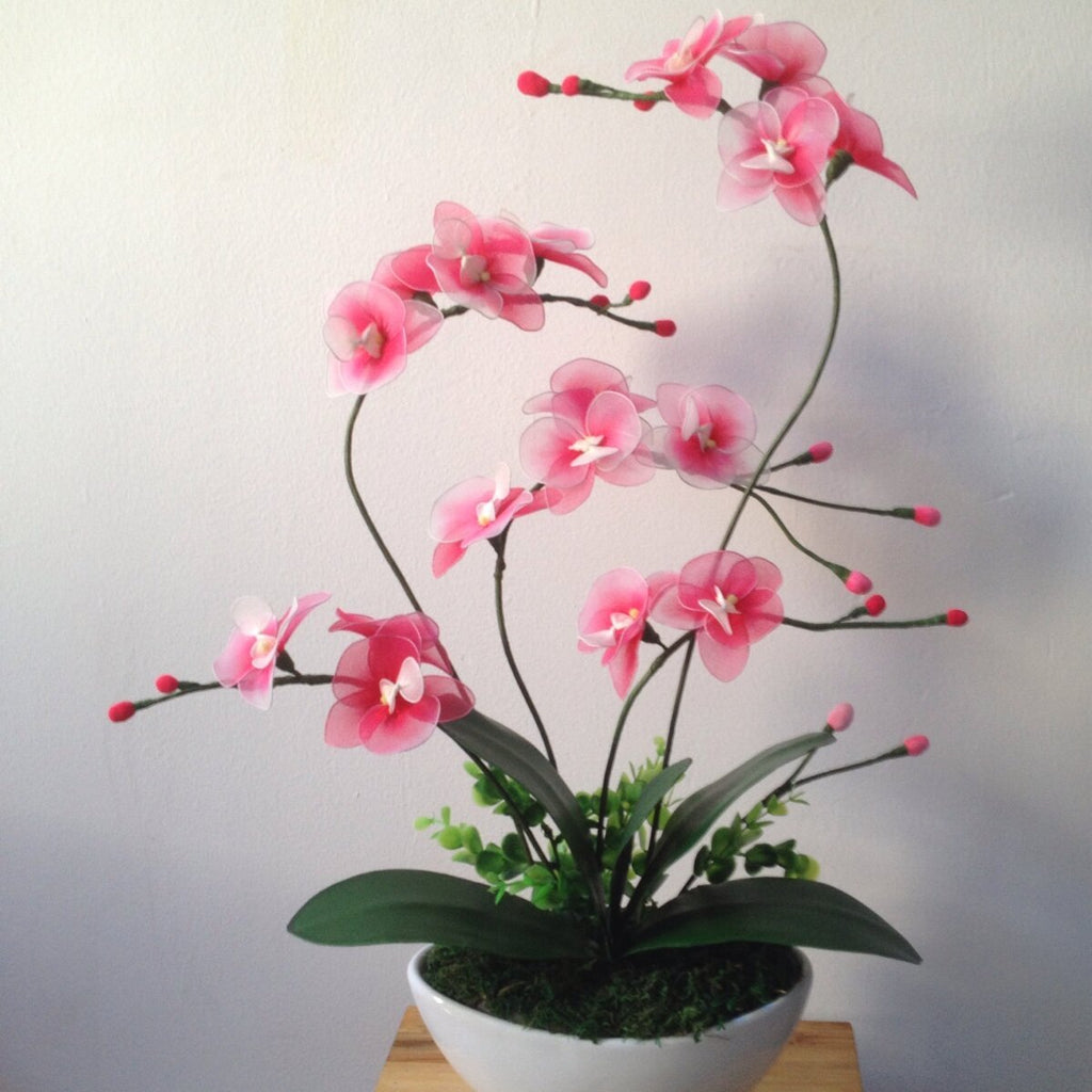 Pink artificial orchid arrangement in a white pot with green leaves and moss