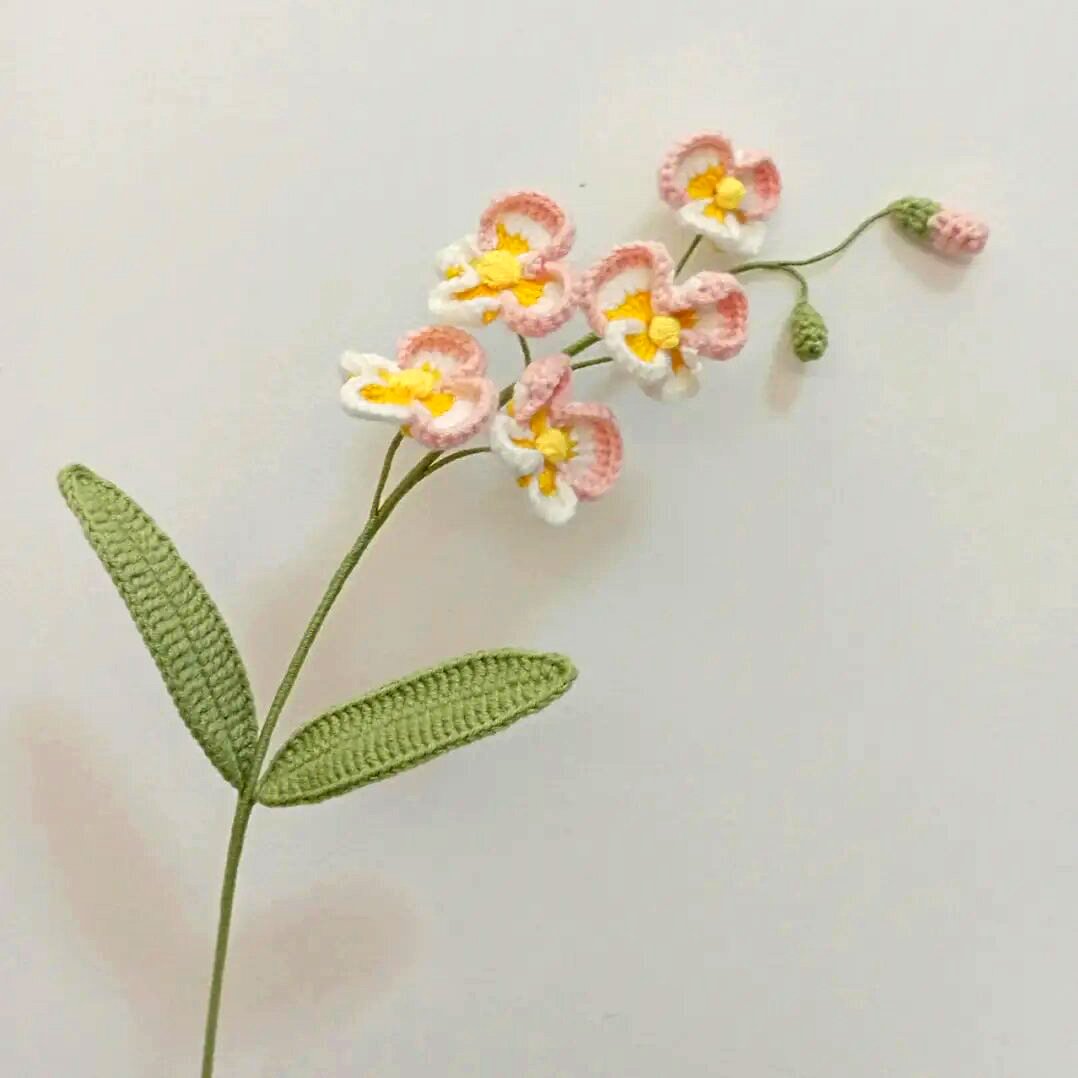 Crocheted pink and white orchid stem with green leaves on a white background