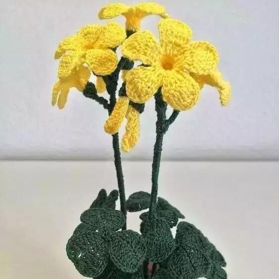 Crocheted yellow flowers with green stems and leaves against a white background.