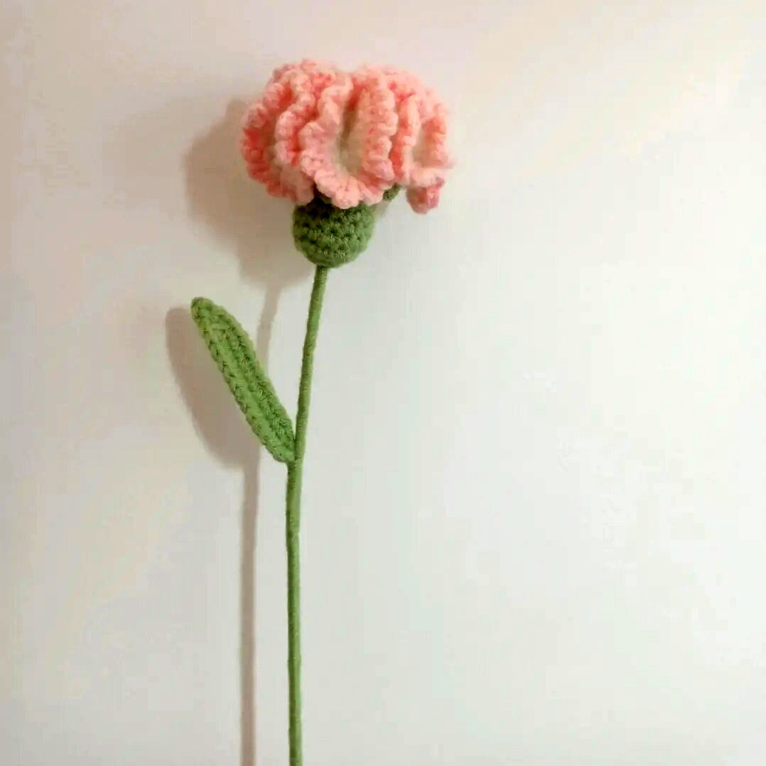 Crocheted pink flower with green stem and leaf against a white background