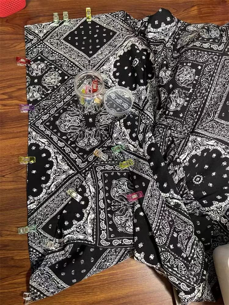 Assortment of colorful sewing clips holding black and white paisley fabric together, with a clear container of clips in the center.