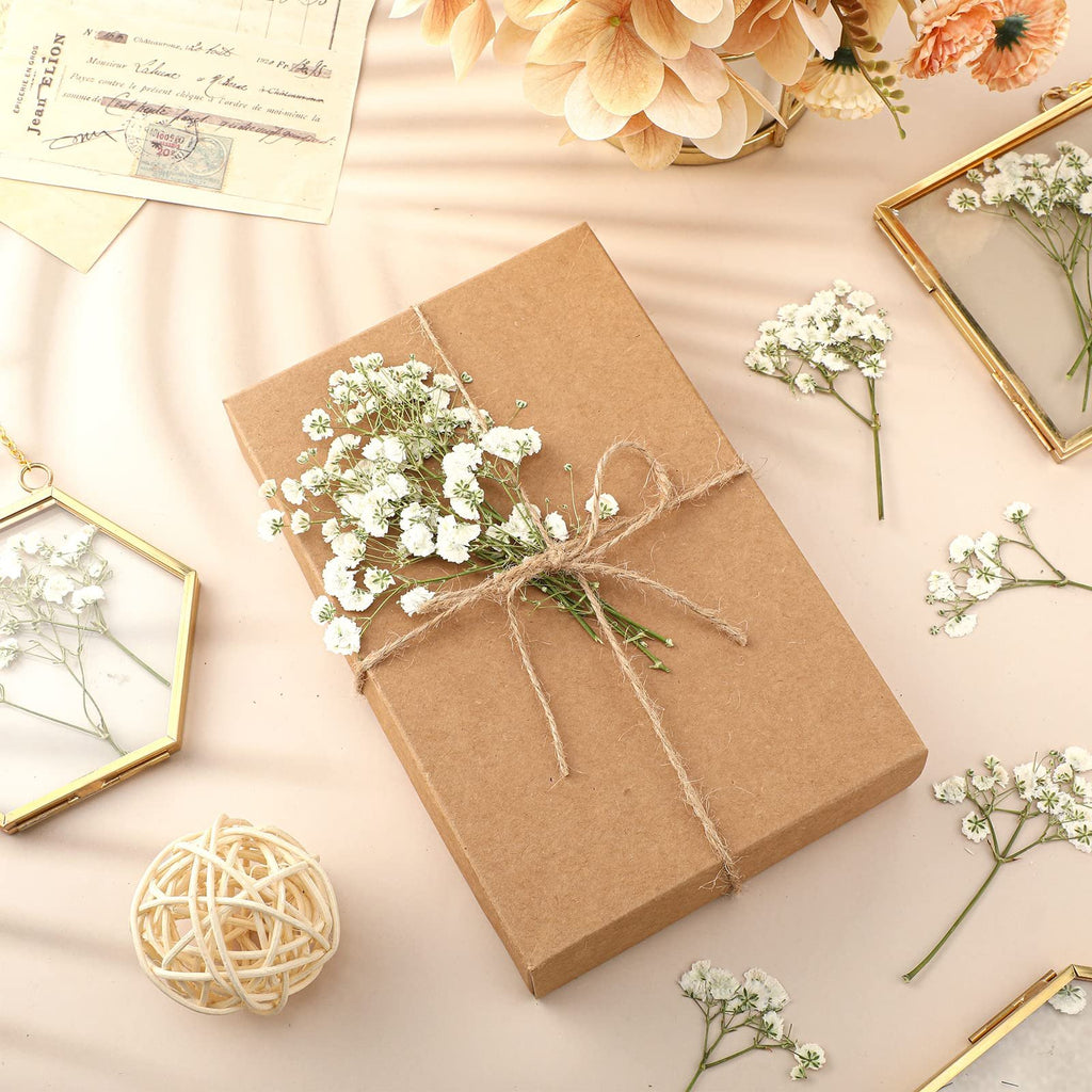 Brown gift box tied with twine and decorated with dried baby's breath flowers, surrounded by more flowers and decorative frames.