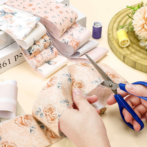 Hands cutting pink floral fabric strips with scissors, spools of thread and decorative flowers nearby