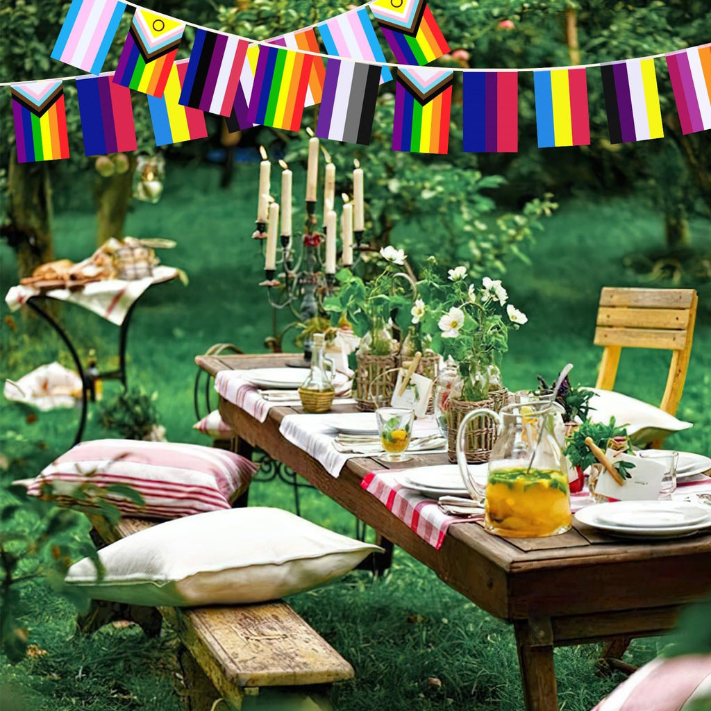 Outdoor table setting with rainbow pride flag bunting strung above, featuring a picnic spread and drinks.