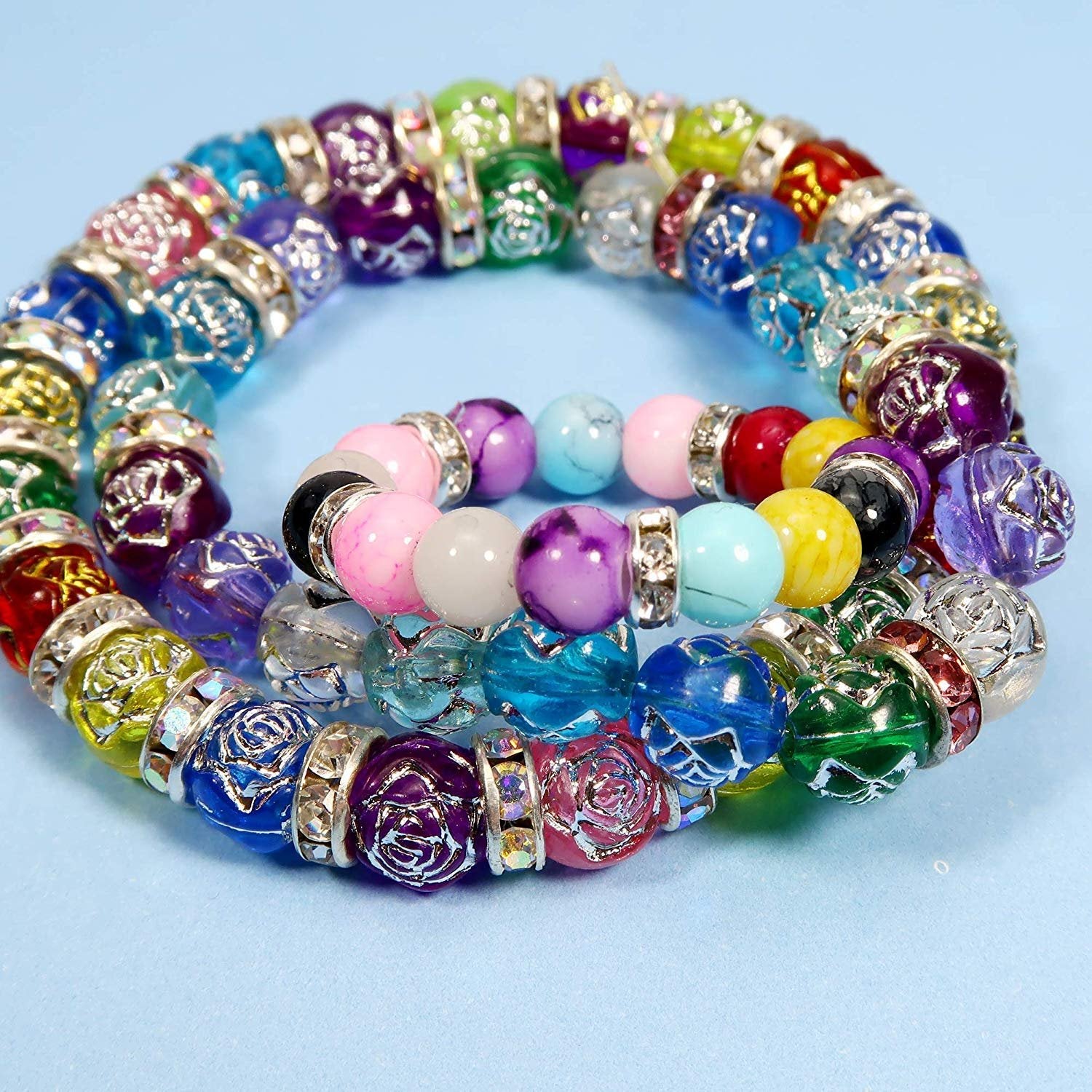 Colorful rondelle spacer beads with rose designs and clear rhinestone accents arranged in two strands on a light blue background.