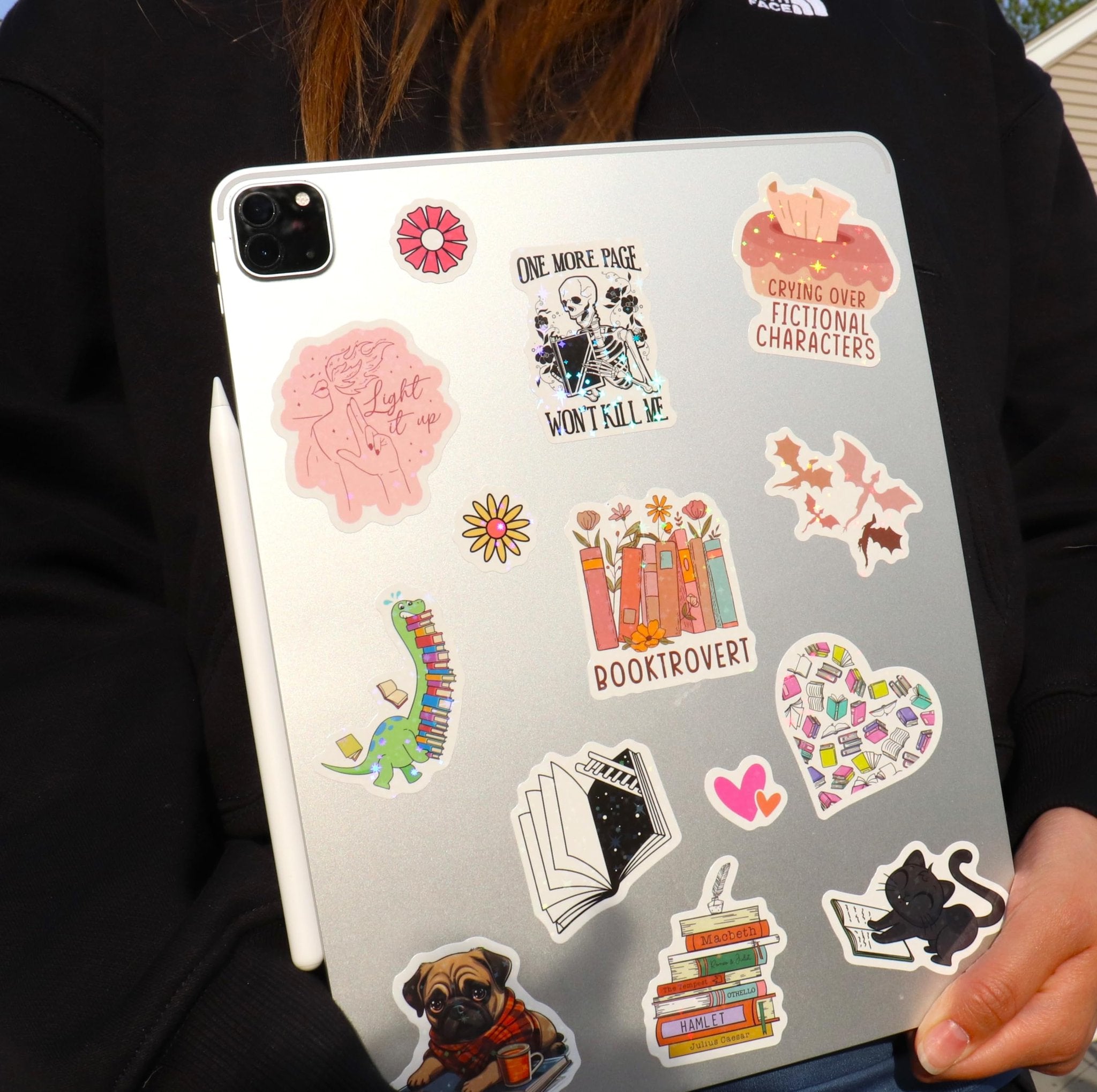 Collection of book-themed vinyl stickers applied to a tablet, featuring designs like a skeleton reading, a dinosaur with books, and a cat reading.