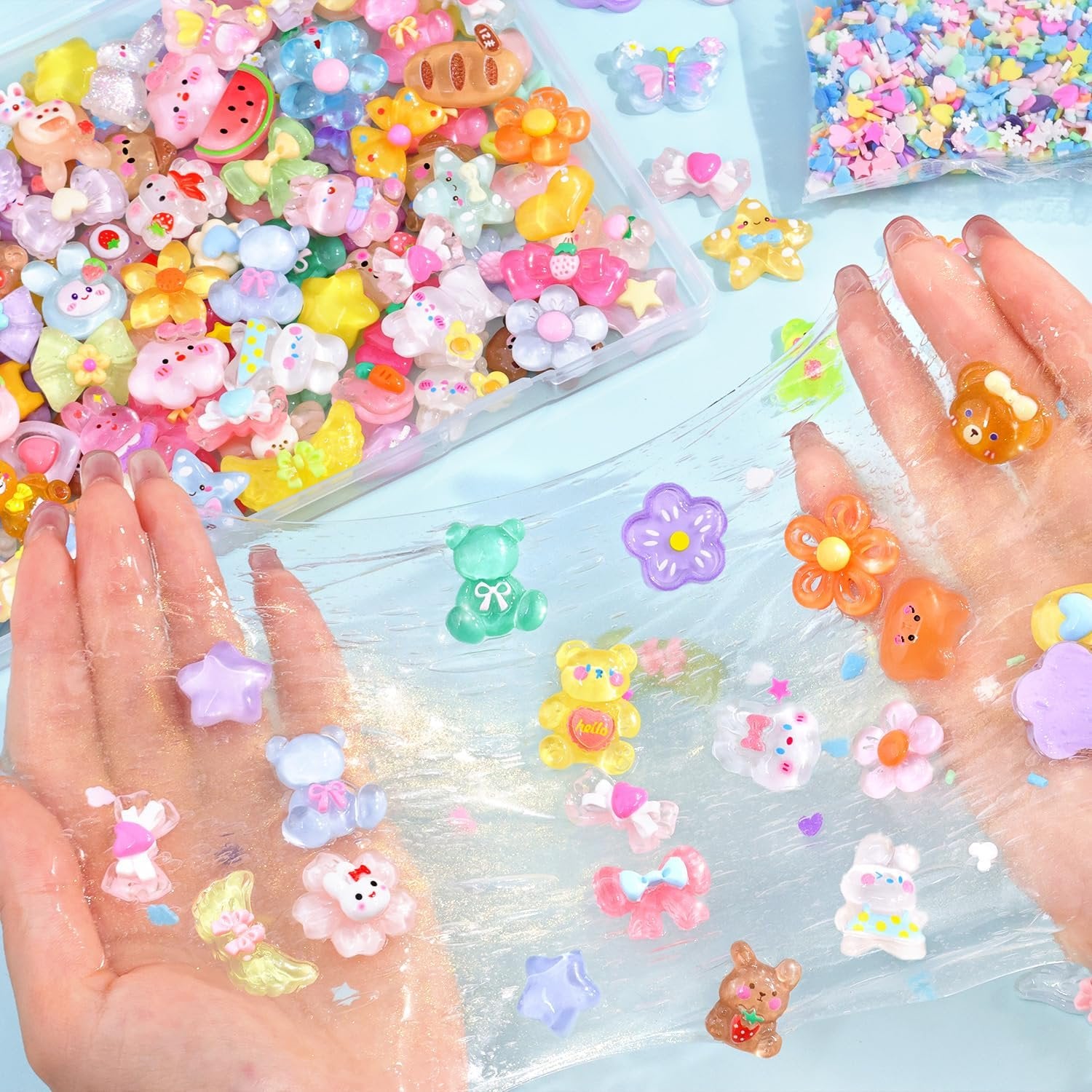 Assorted kawaii resin charms including bears, flowers, and fruit scattered on slime held by hands.