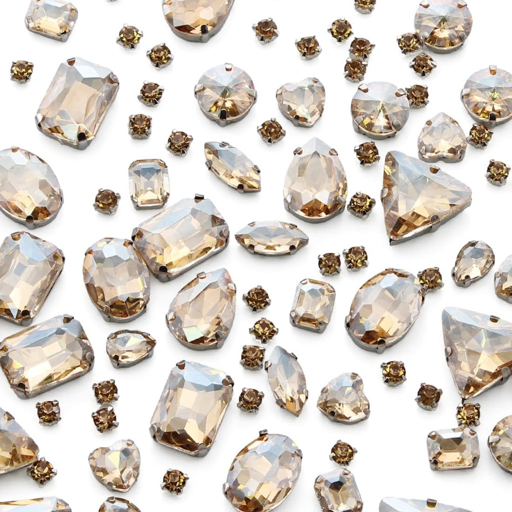Assortment of champagne colored glass rhinestones with silver claw settings in various shapes and sizes scattered on a white background.
