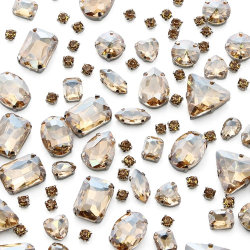 Assortment of champagne colored glass rhinestones with silver claw settings in various shapes and sizes scattered on a white background.