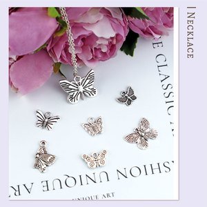 Assortment of seven silver-tone butterfly charms for jewelry making, arranged on a flat surface with flowers.