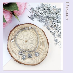 Mixed Tibetan silver alloy charm pendants and a bracelet on a wooden slice, with pink flowers in the background.