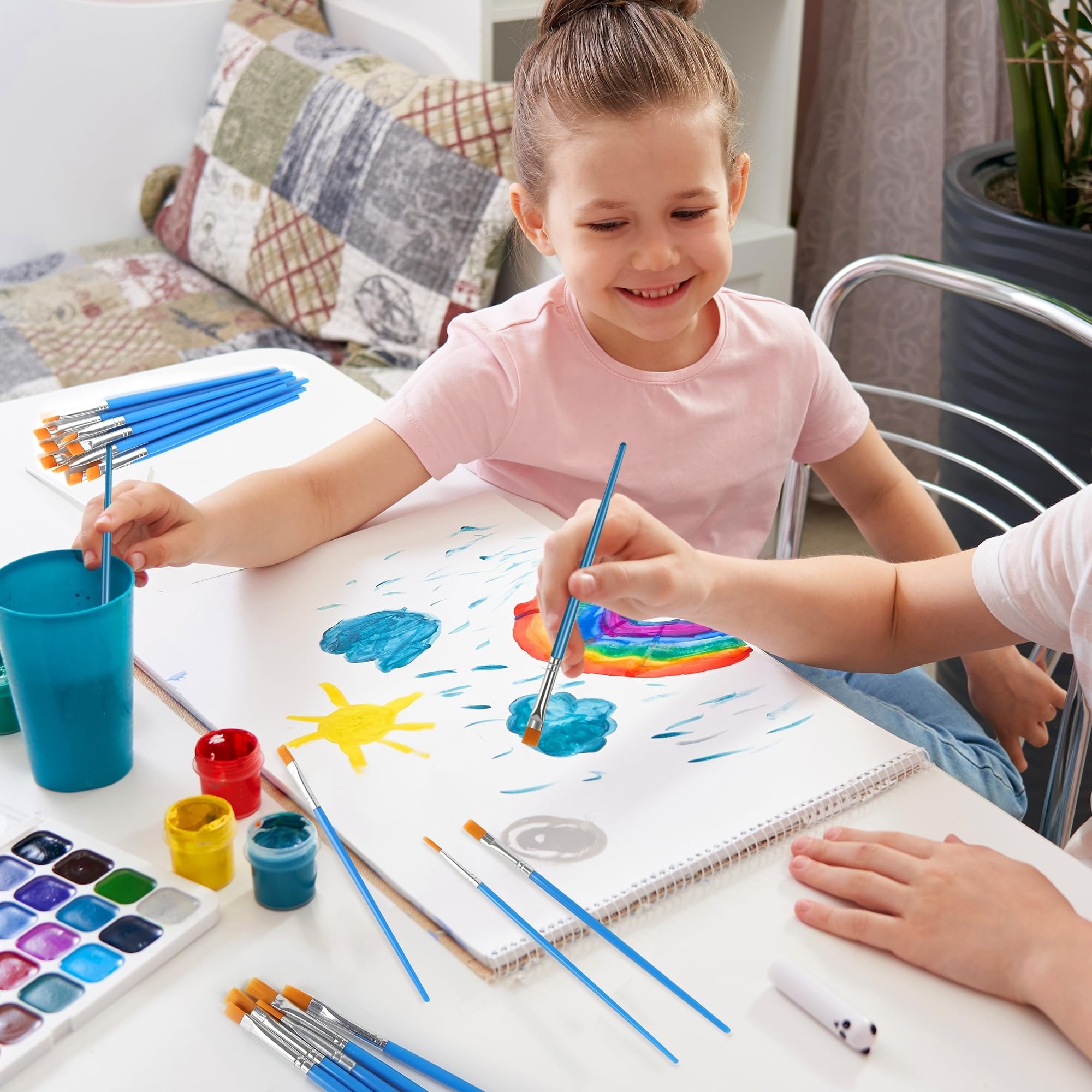 Two children painting a picture with watercolor paints and brushes on a white table.