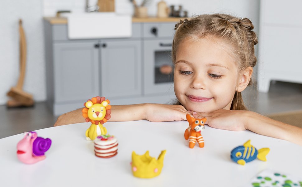 Young girl looking at clay animal figures including a lion, fox, and fish on a white table.