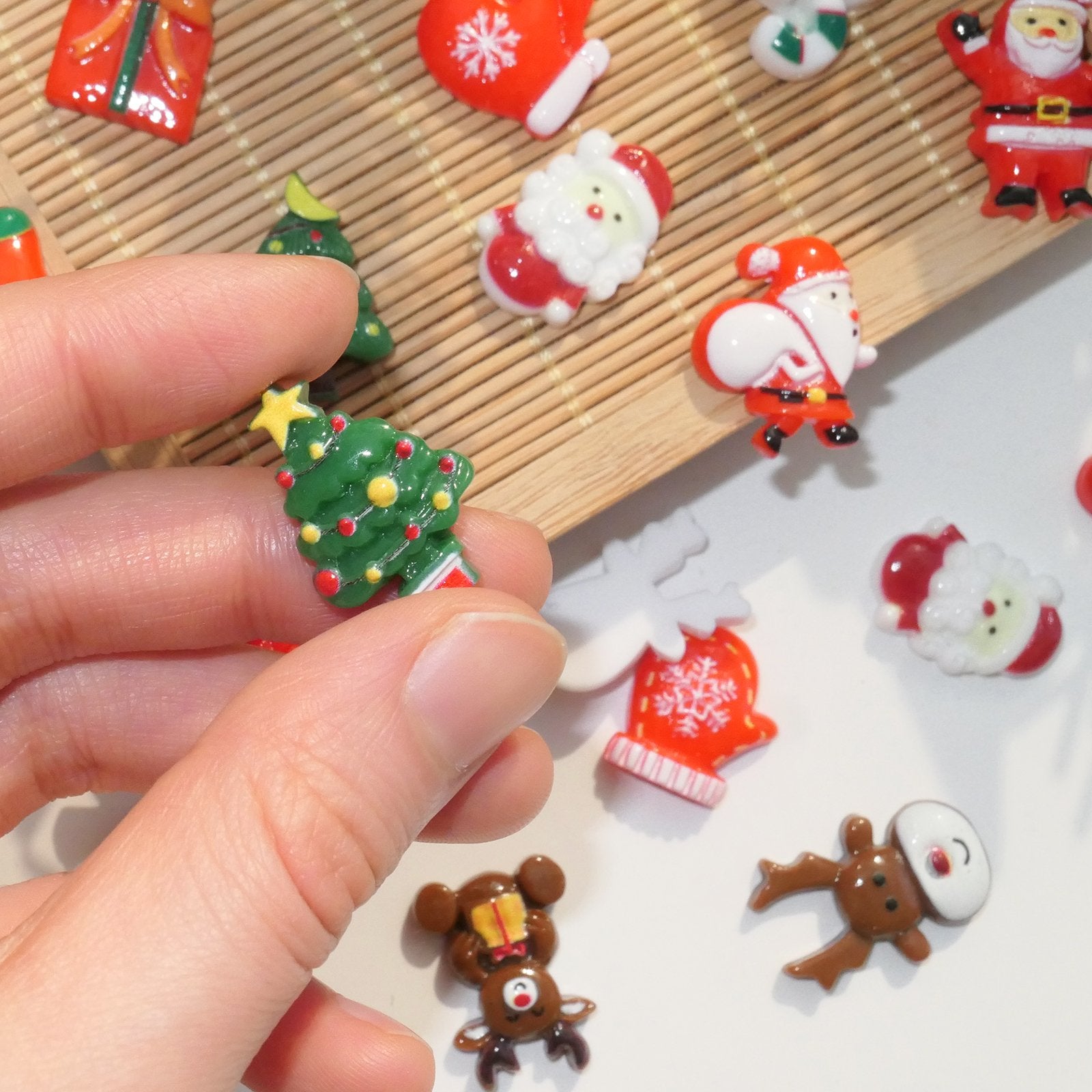 Hand holding a miniature resin Christmas tree charm with red and yellow ornaments and a yellow star.