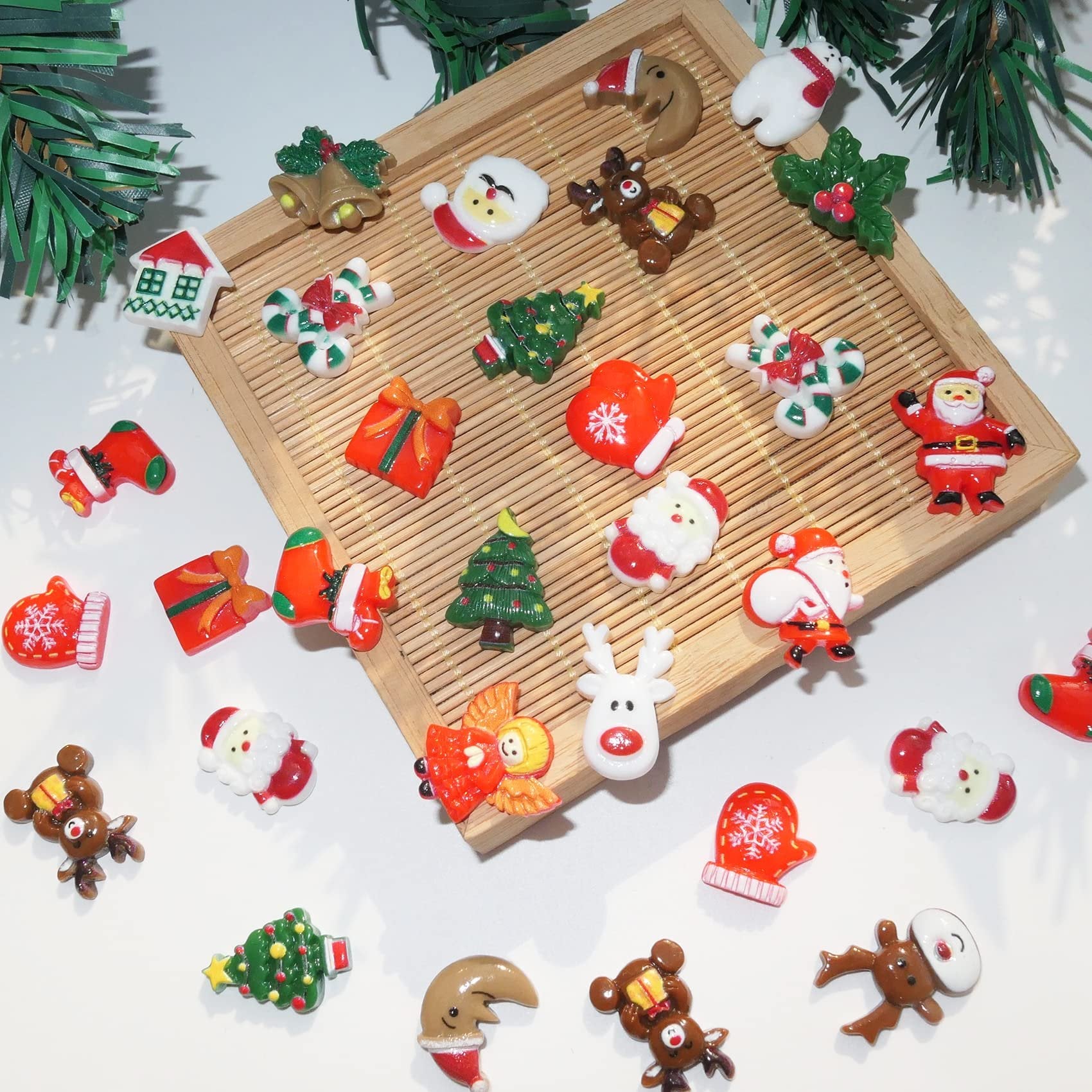 Assorted 3D Christmas resin charms including Santa, reindeer, Christmas trees, bells, and stockings scattered on a white surface with a bamboo tray.