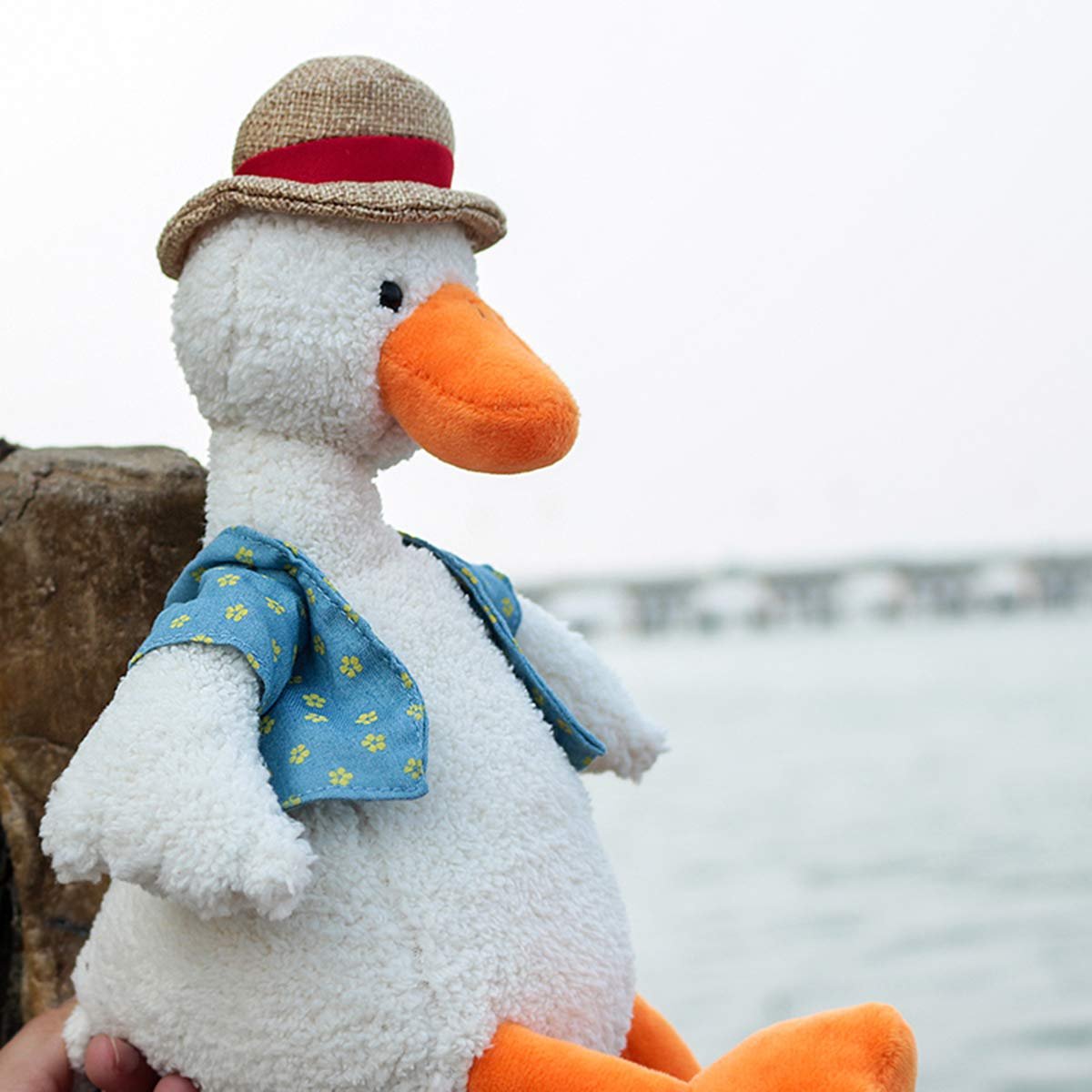 Plush duck wearing a hat and vest, sitting outdoors with a blurred background.