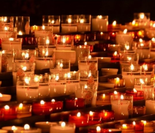 Rows of lit votive candles in glass holders, some with decorative images, creating a warm glow.