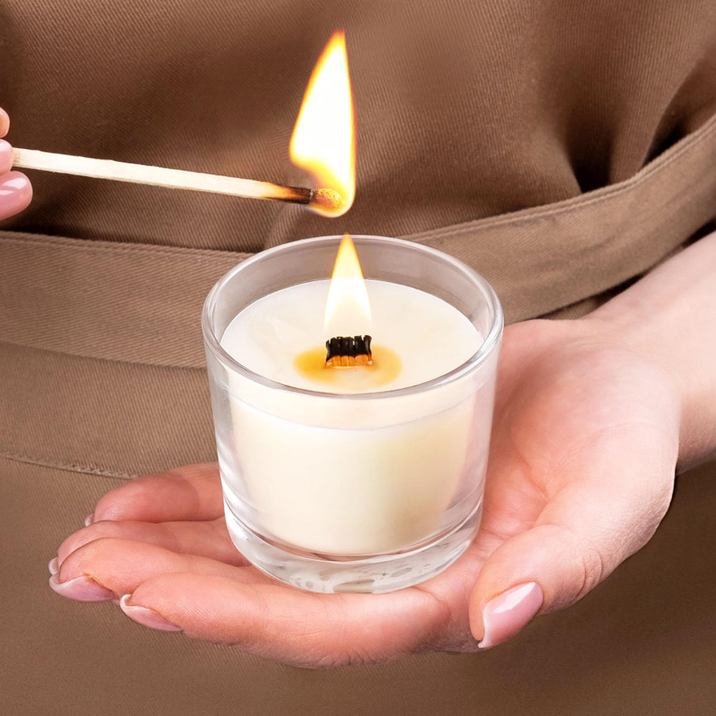 Hands lighting a wooden candle wick in a glass jar with a lit match