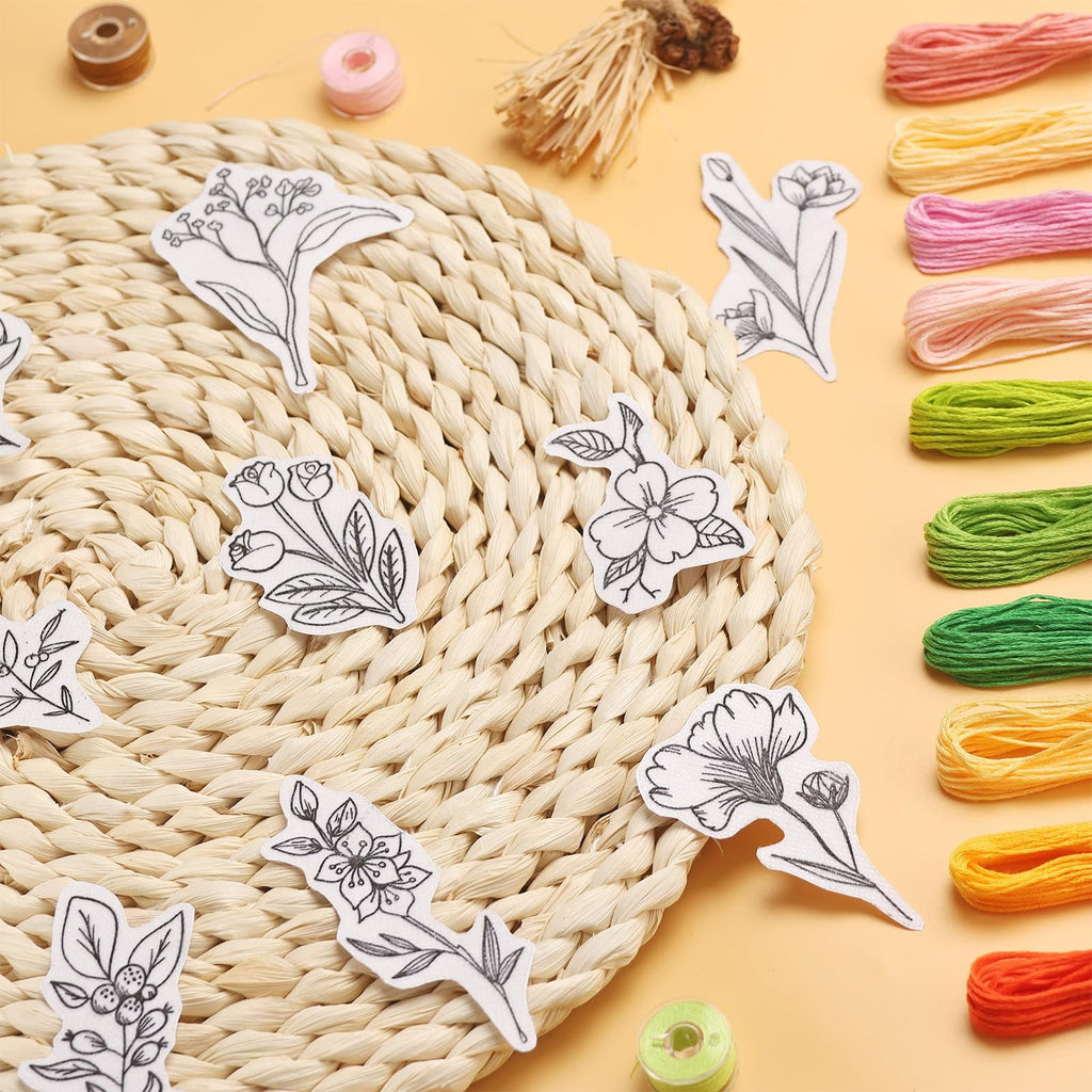 Assortment of pre-printed floral embroidery stabilizer patterns scattered on a woven mat with embroidery floss spools.