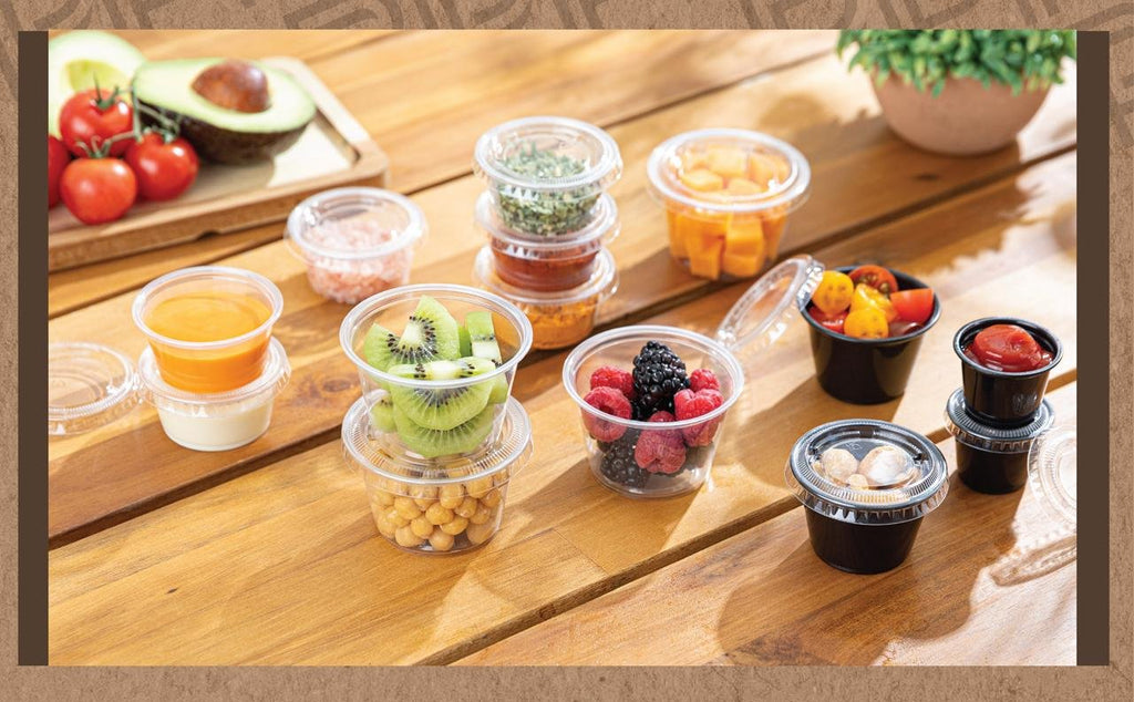 Assortment of clear and black plastic portion cups filled with various foods and ingredients on a wooden table.