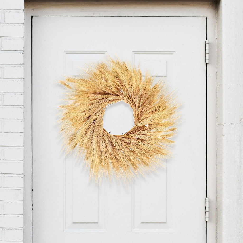 Dried wheat stalk wreath hanging on a white door, showcasing natural golden stalks arranged in a circular shape.