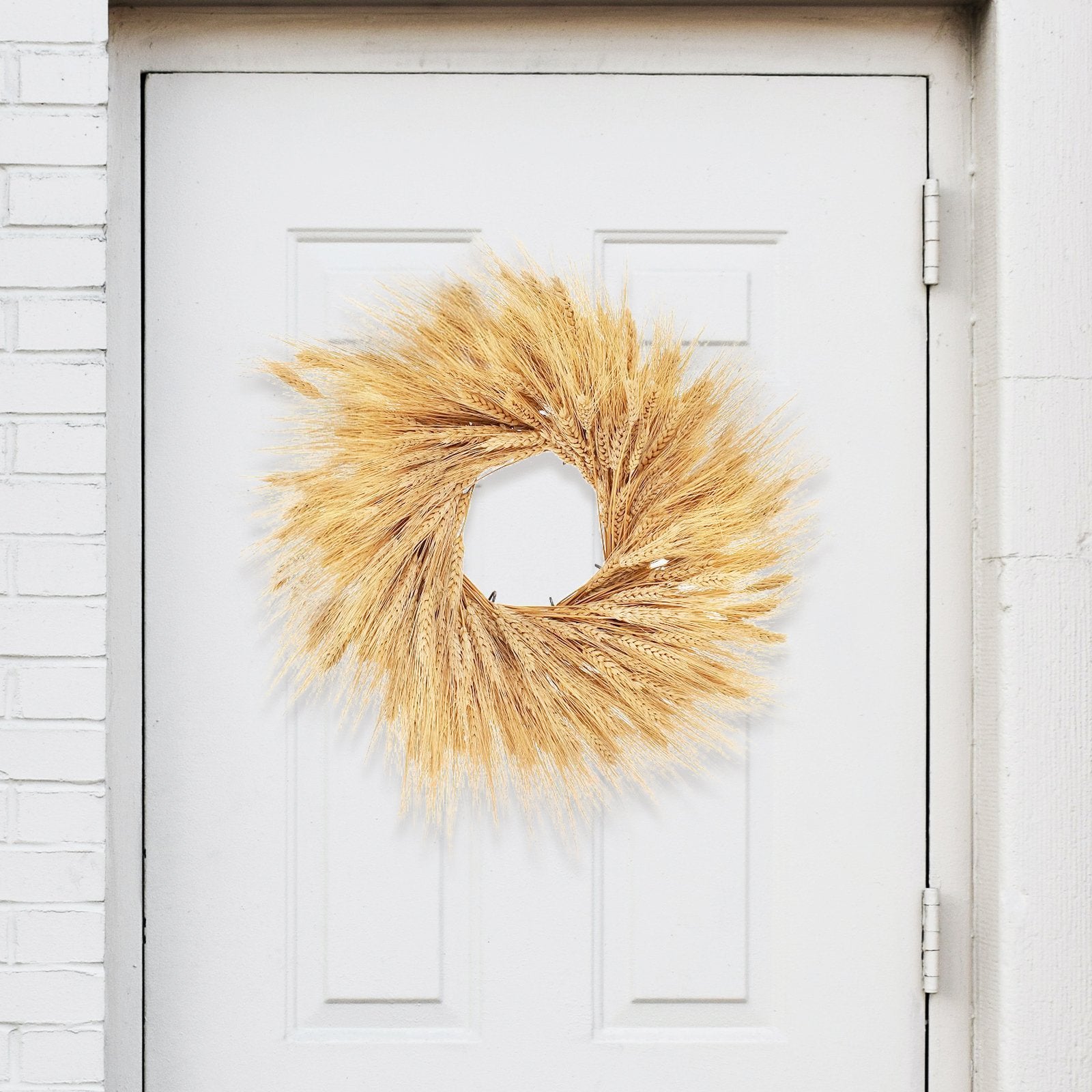 Dried wheat stalk wreath hanging on a white door, showcasing natural golden stalks arranged in a circular shape.