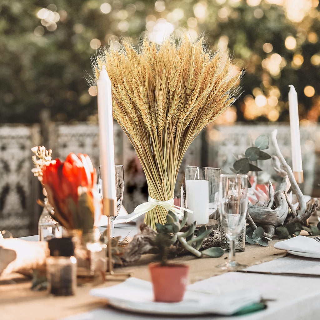 Dried wheat stalks arranged as a centerpiece on a table with candles and flowers.