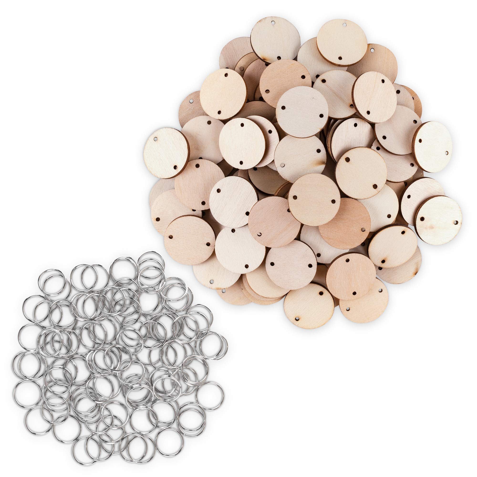Pile of unfinished wooden circles with holes and a separate pile of silver key rings on a white background.