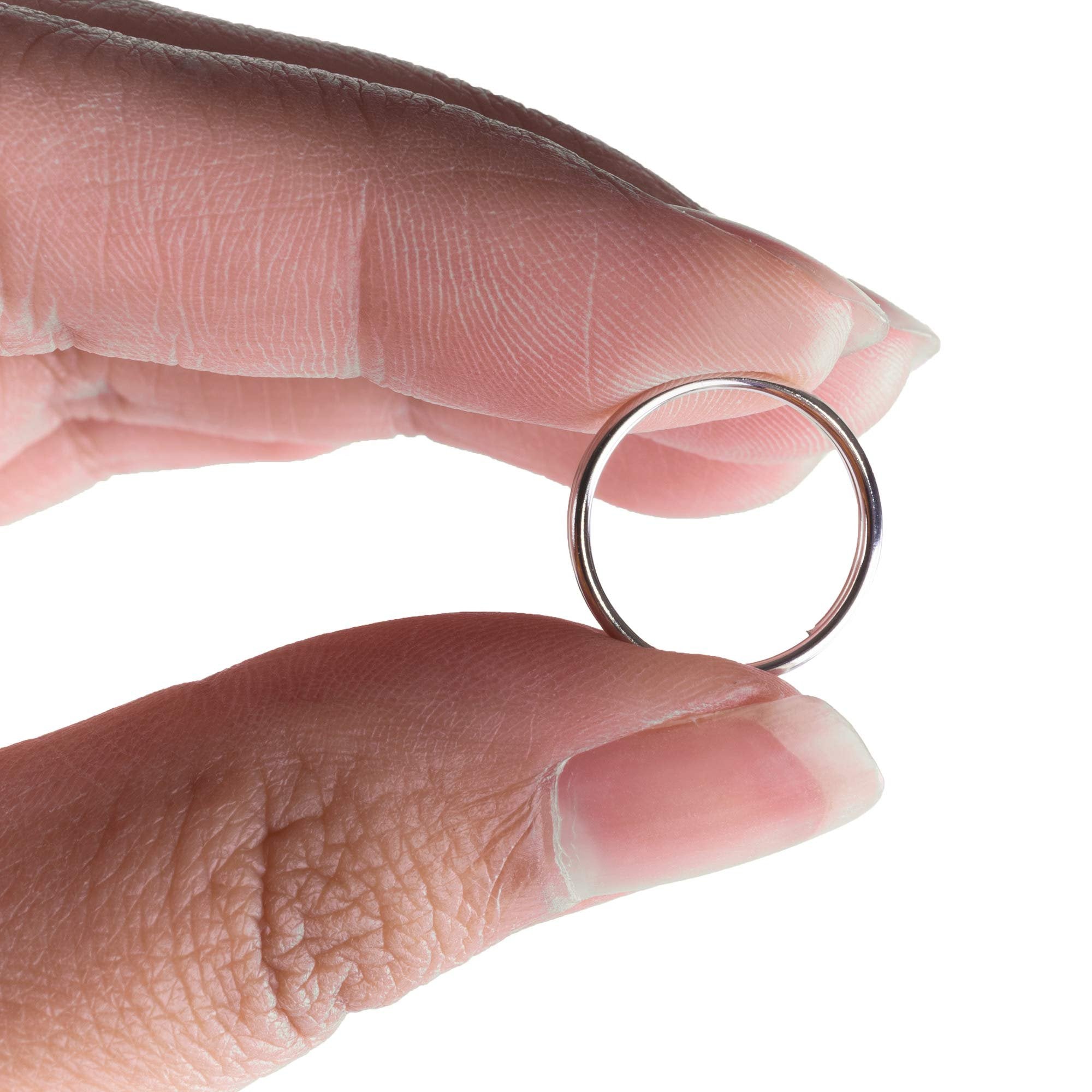 Close-up of a person's fingers holding a single silver key ring against a white background.
