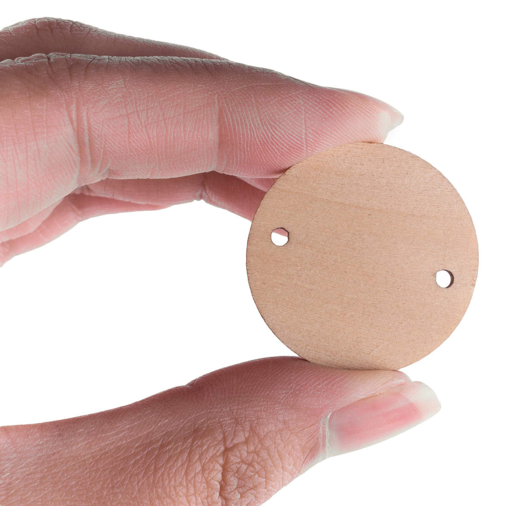 Fingers holding a 1.2-inch unfinished wooden round disc with two pre-drilled holes for crafts.