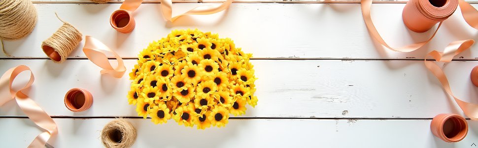 A large pile of 100 yellow artificial sunflower heads with brown centers, arranged on a white wooden surface with spools of twine and peach ribbon.