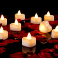 Heart-shaped LED tea lights scattered amongst red rose petals on a reflective black surface.