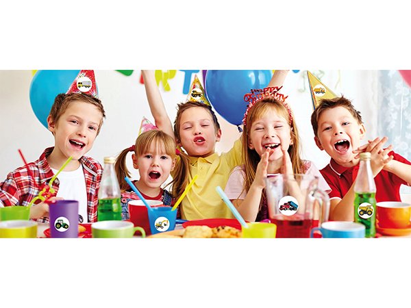 Five children wearing party hats at a table with drinks and snacks, some with cartoon truck stickers on cups.