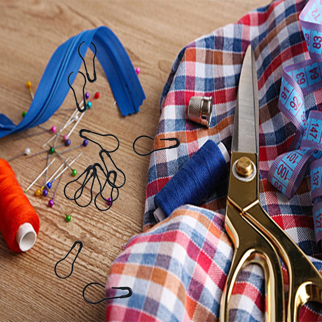 Black metal bulb safety pins scattered with sewing supplies including a blue zipper, thread, scissors, and measuring tape on a wooden surface.